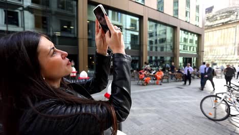 close-up of the face of a pretty young woman tourist taking pictures with her phone of buildings on a central city street in london
