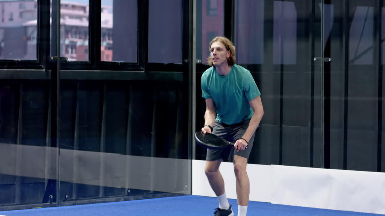 Man playing padel tennis on indoor court, holding racket and focusing on game