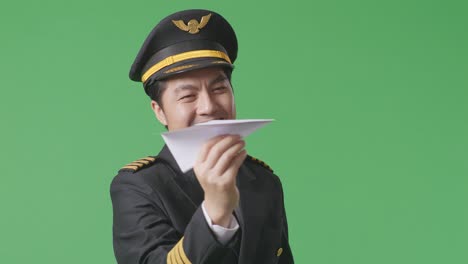 close up of asian man pilot in professional uniform launching paper plane, holding jet model in hands, aviation academy aviator, aircraft captain on green screen background studio