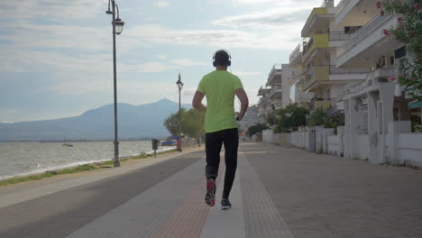 young man in headphones runs on road of city perea greece