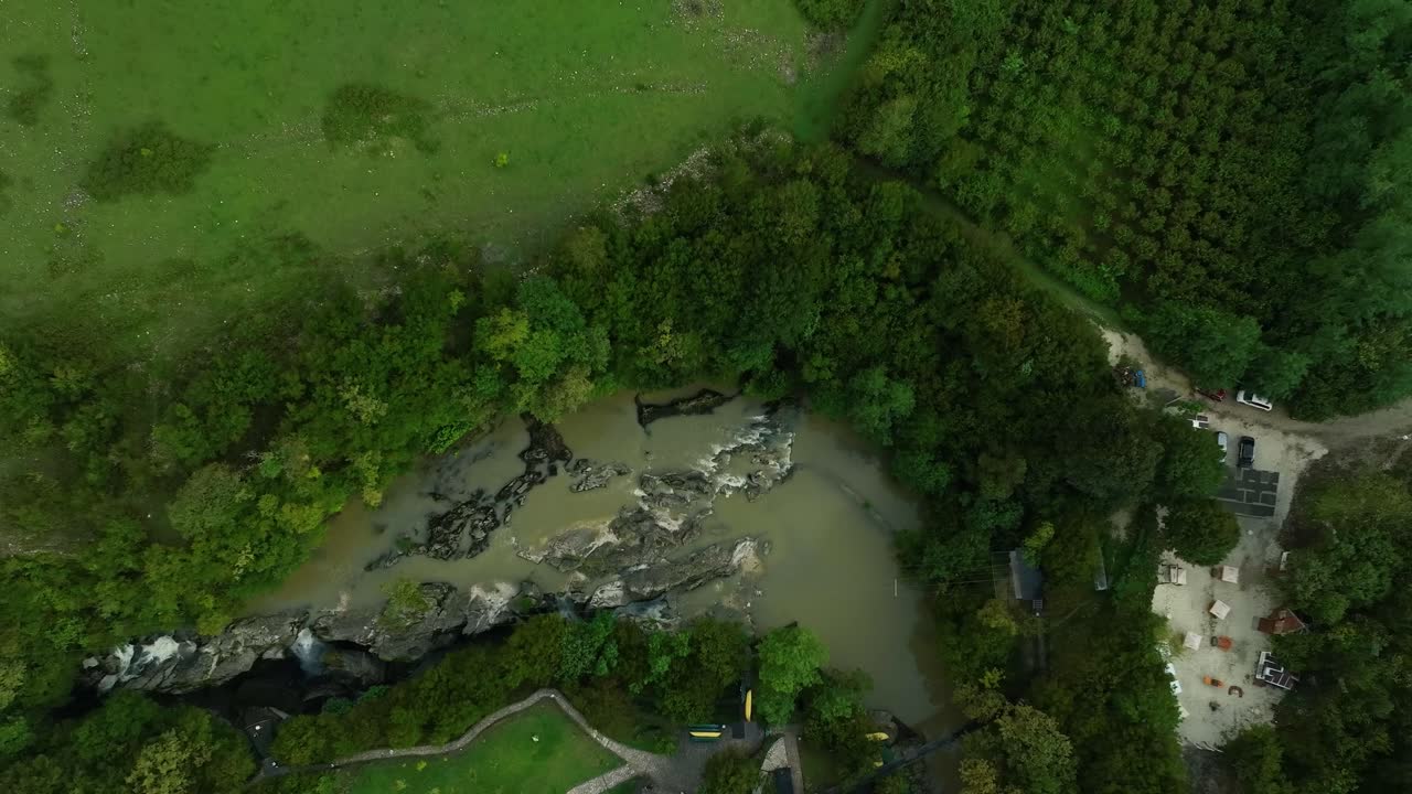 A wide aerial shot of a winding riverbed cutting through thick forest with rocky edges, highlighting the raw beauty of an untouched natural environment