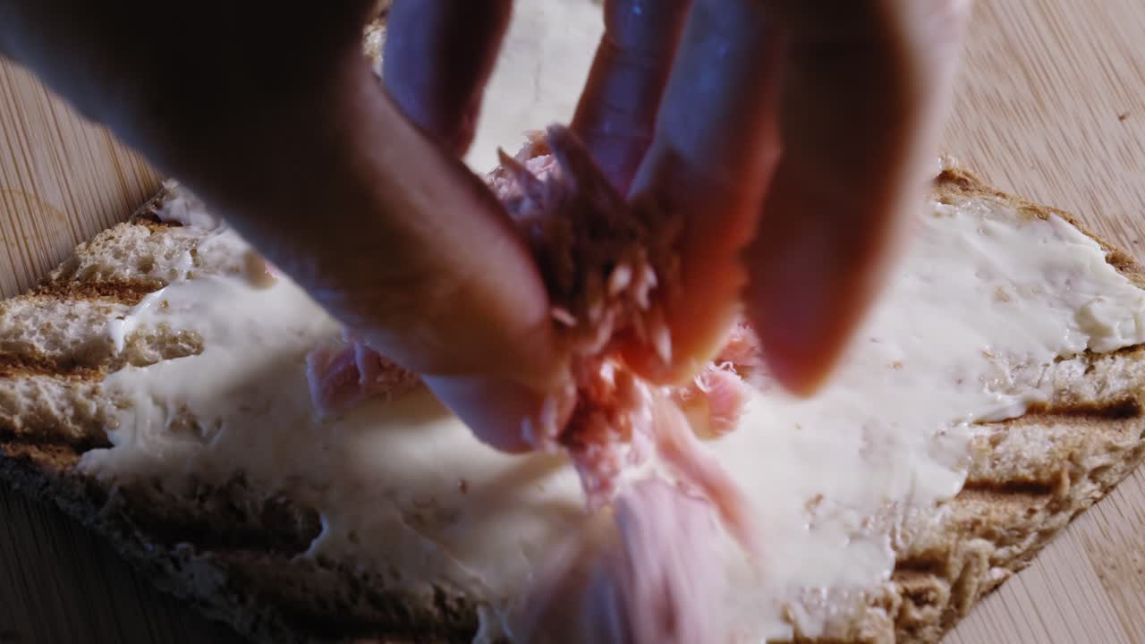 녹은 치즈 스프레드를 곁들인 곡물 토스트 빵 한 조각에 참치 플레이크를 손으로 얹습니다.