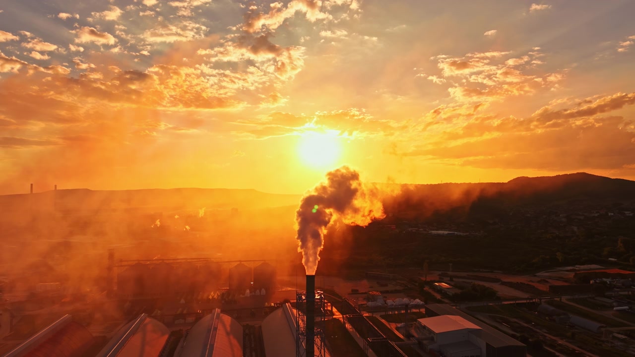 Sunset over industrial area with smoke rising from factory chimneys while the sky shows bright orange and yellow colors