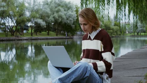mujer trabajando en una computadora portátil en un parque junto a un río