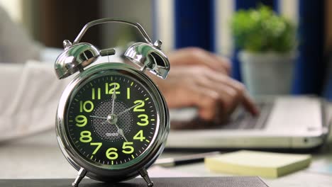 man finishing work on a laptop with an alarm clock