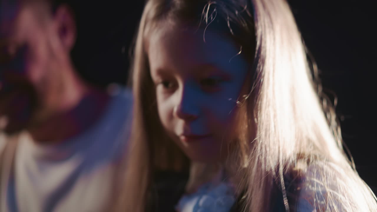 소녀는 스튜디오 클로즈업에서 신디사이저를 연주합니다. 결단력있는 소녀는 근처에 있는 교사와 함께 키보드 기술을 연습합니다. 음악 지식을 연습으로 번역합니다.