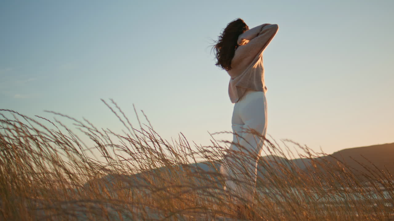 Woman running sandy hill covered dry grass. Brunette contemplating golden sunset