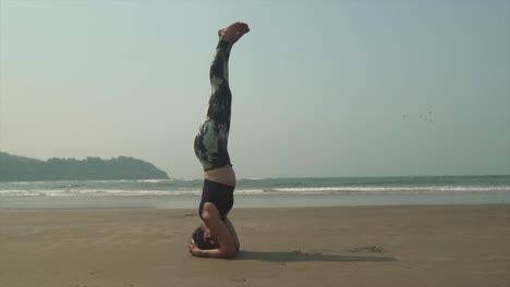 在溫暖的熱帶海灘上,一個健康的年輕女人正在練習<unk>頭站,salamba shirshasana