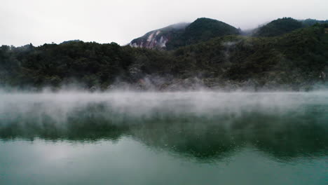 fly through stream hovering over surface of volcanic lake towards lush forest in new zealand