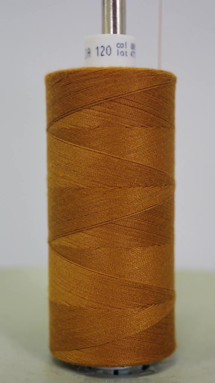 Macro close up of a mustard yellow sewing thread cone mounted on a metal spindle