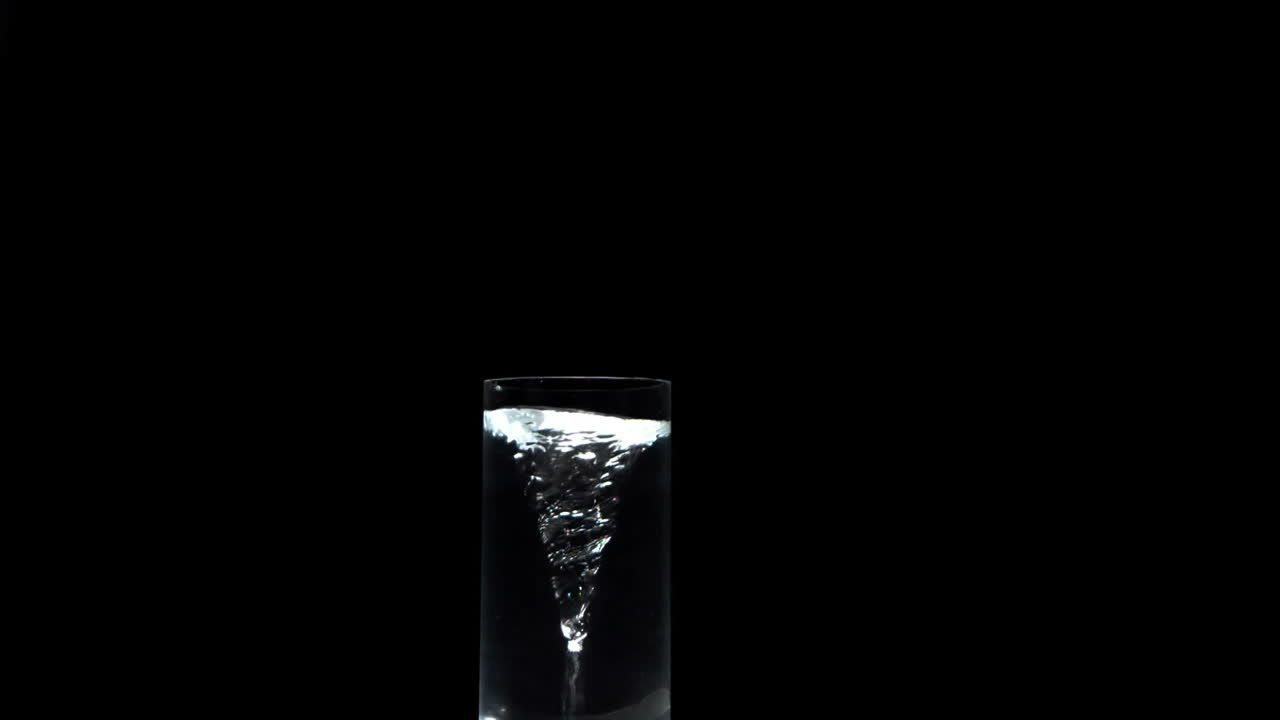 Vortice in un bicchiere d'acqua su una superficie nera.