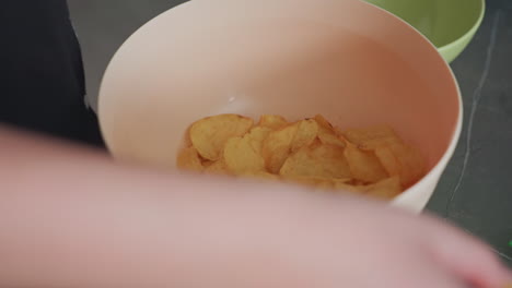 close up of crispy plantain chips falling into bowl on kitchen counter, snack food preparation, golden fried chips texture, casual home cooking moment, healthy crunchy treat