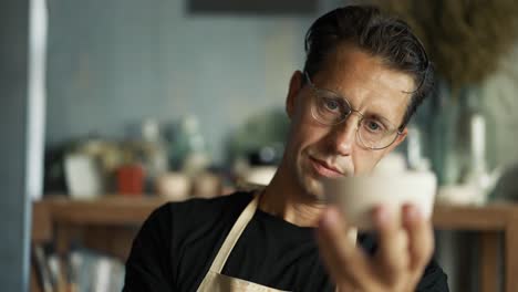 Glücklicher-Junger-Töpfer-Mit-Brille-Und-Schwarzem-T-Shirt-Untersucht-Seine-Arbeit.-Nahaufnahme.-Beurteilung-Ihrer-Erfolge