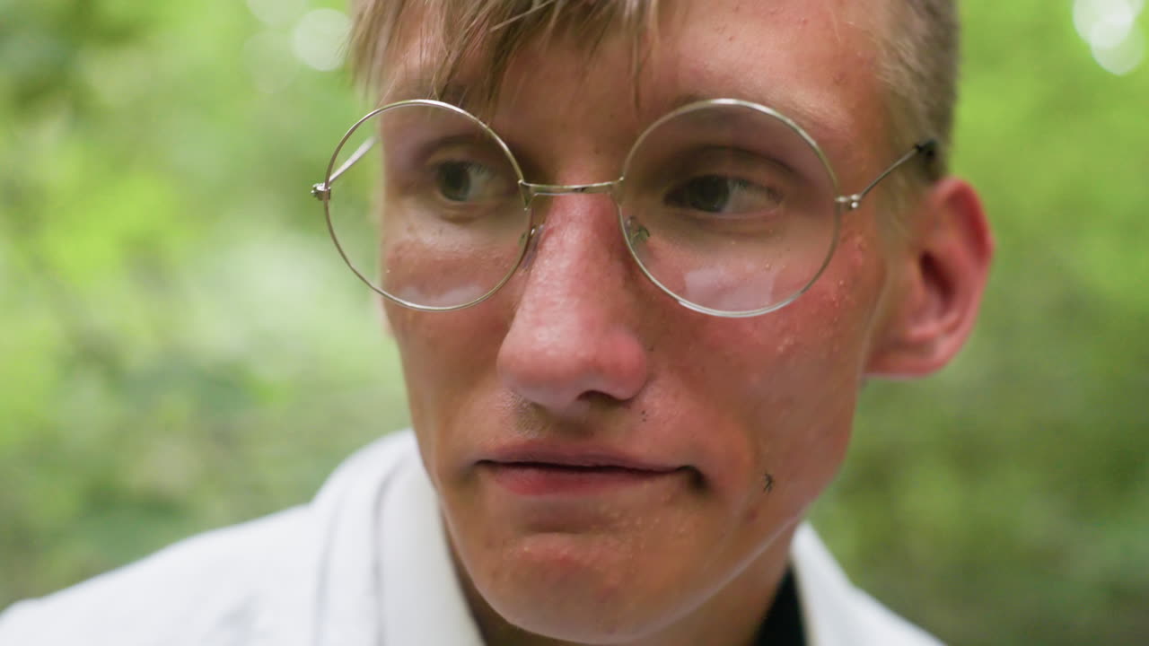 Portrait view botany student in white shirt removing glasses in forest with tired expression surrounded by blurred green trees, reflecting fatigue and stress during outdoor research