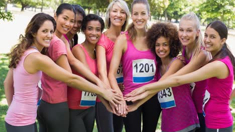 Diverse-group-of-smiling-women-staking-hands-outdoors-in-the-sun-from-below