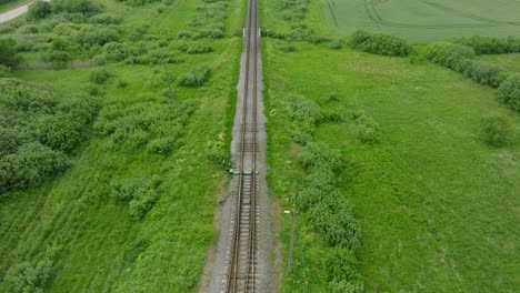 aerial birdseye view of empty railroad train tracks, countryside scenery, fresh green forest on the side, overcast cloudy summer day, wide drone shot moving forward