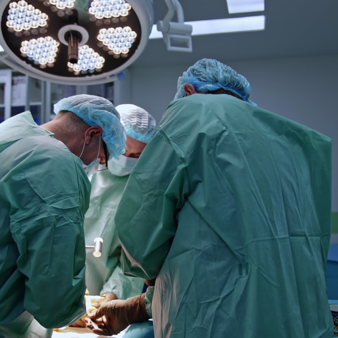 Chief surgeon uses a mallet and chisel in orthopedic operation. Two doctors assisting the professional