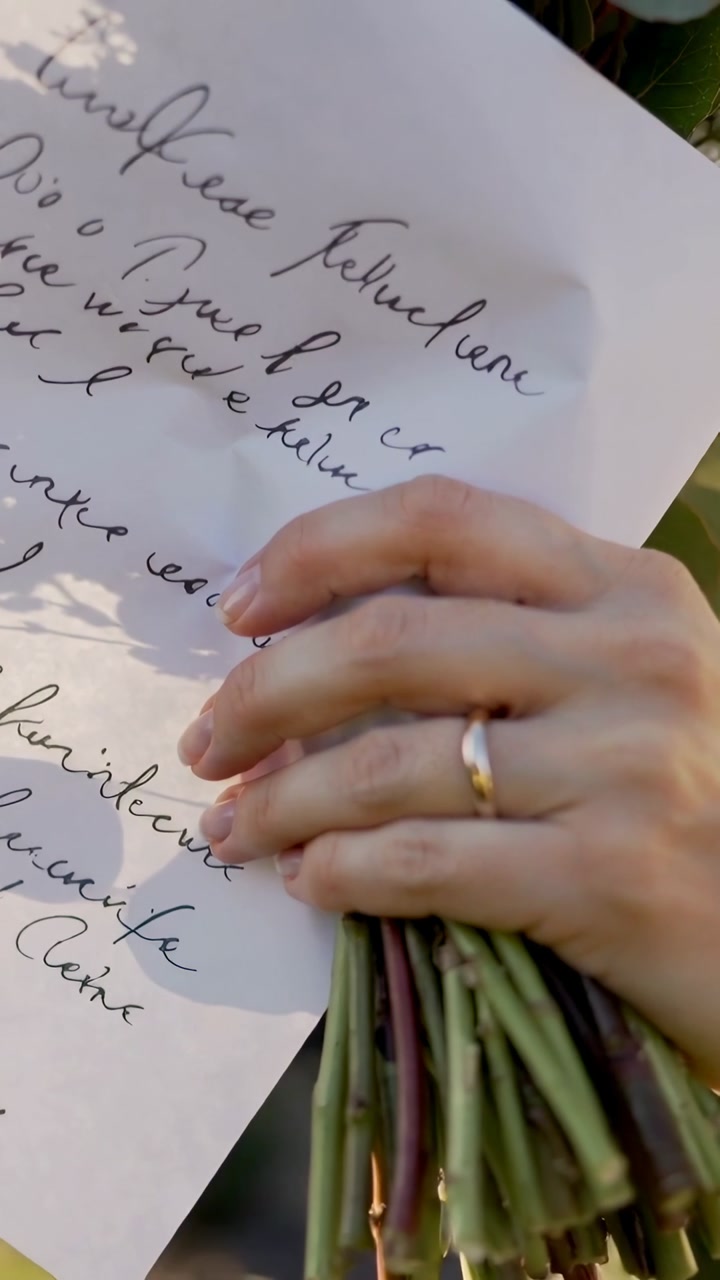 Vertical video: Hand entering frame adjusting written note in sunny garden to steady bouquet stems