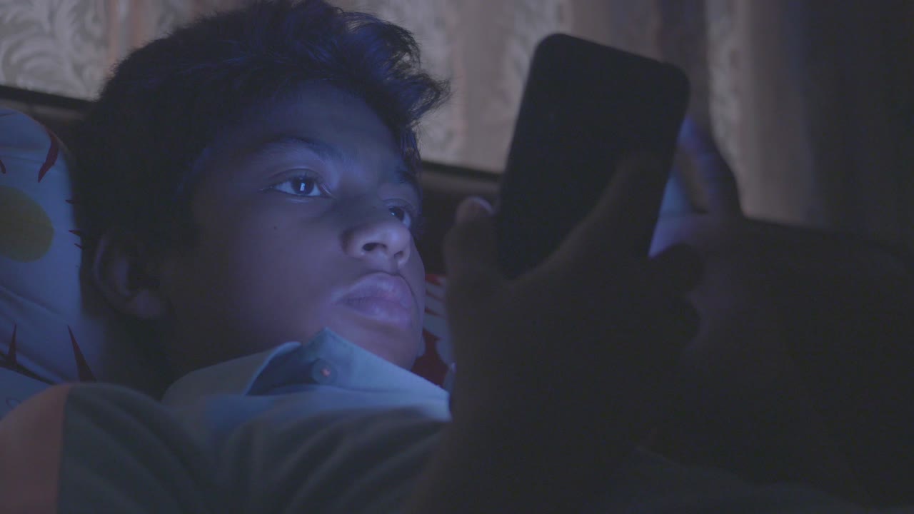 Teenage boy sitting on sofa using smart phone at night