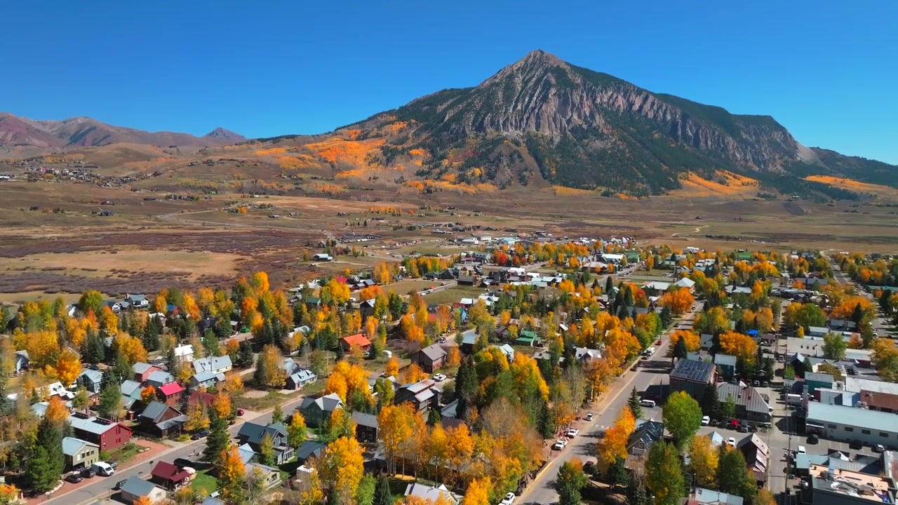 Estância de esqui da cidade montanhosa de Mount Crested Butte, Passo Kebler Ohio, drone aéreo, manhã no Colorado, vibrantes árvores de álamo tremedor, cores de pico de outono em tons de castanho-avermelhado, Floresta Nacional de Gunnison, céu azul ensolarado, panorâmica frontal ascendente.