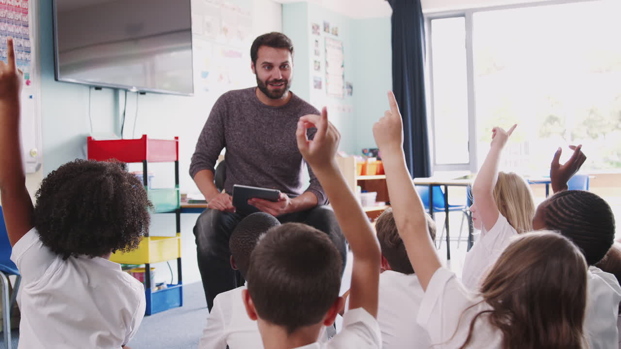 maestro masculino con una tableta digital enseña a un grupo de alumnos de primaria uniformados en el aula de la escuela