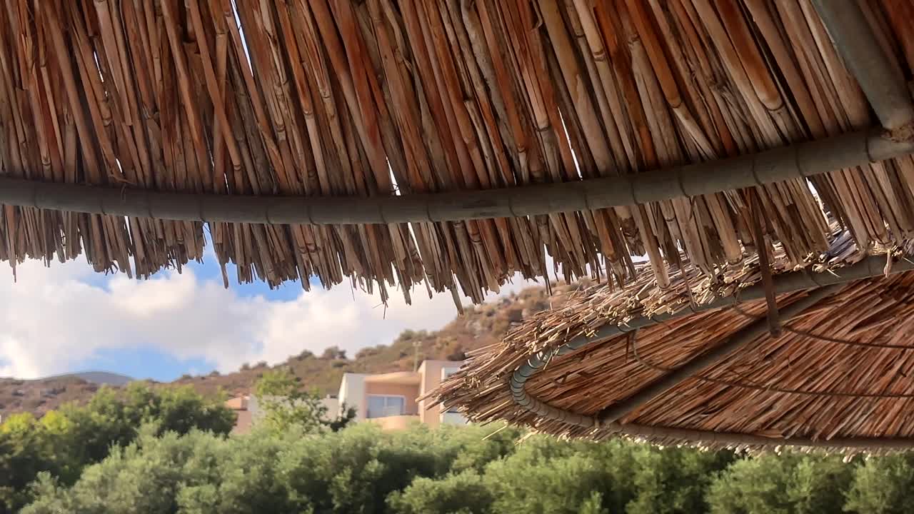 Close up of a thatched umbrella against a backdrop of greenery and distant hills