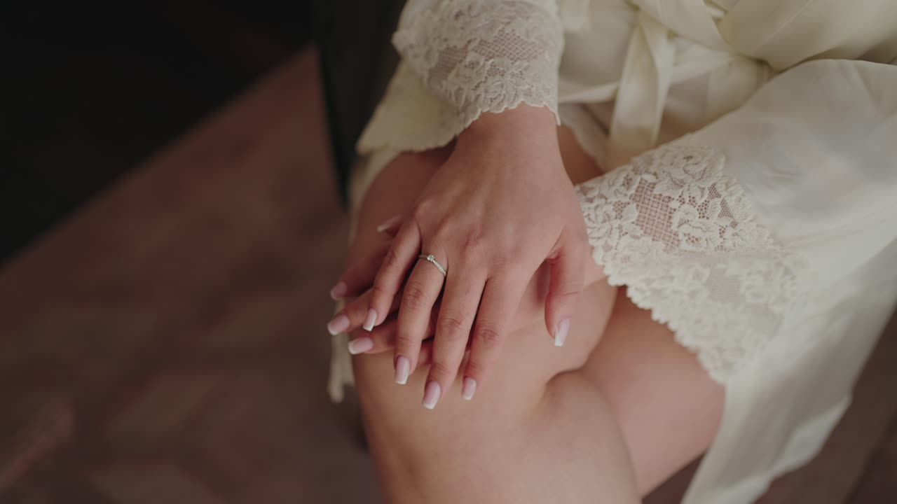 Close up of a bride’s hands resting on her lap, wearing an elegant engagement ring