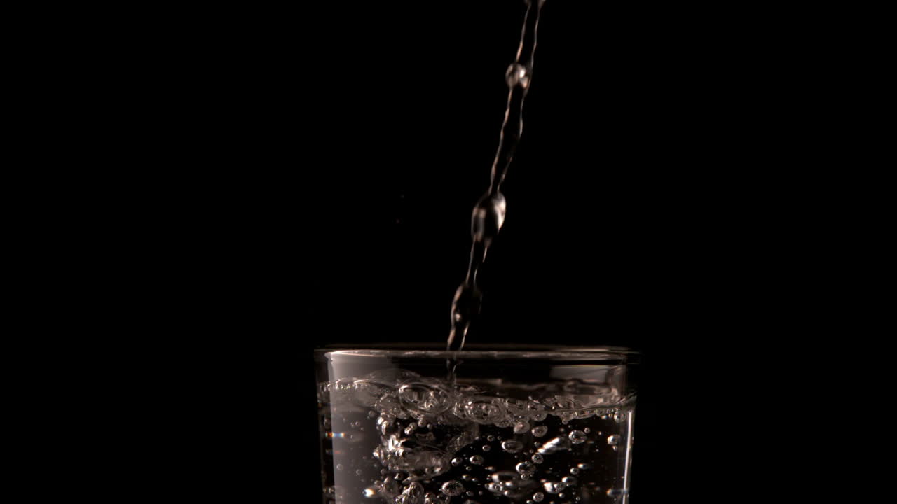 Water pouring into glass on black background