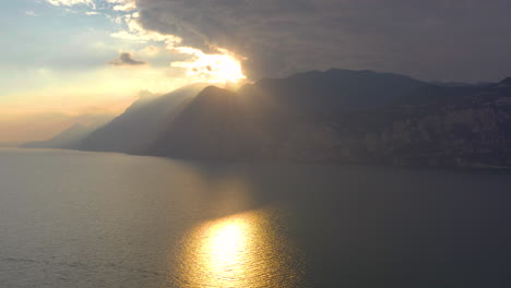 Toma-Aérea-Del-Sol-De-La-Puesta-Del-Sol-Rompiendo-Las-Nubes-Y-Derramando-Una-Luz-Dorada-Asombrosa,-Cálida,-Suave-Y-Dorada-Sobre-Las-Majestuosas-Montañas