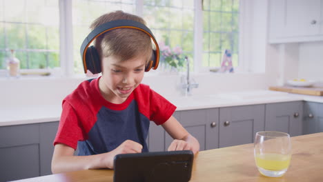 boy at home in kitchen watching movie or show on mobile phone wearing wireless headphones