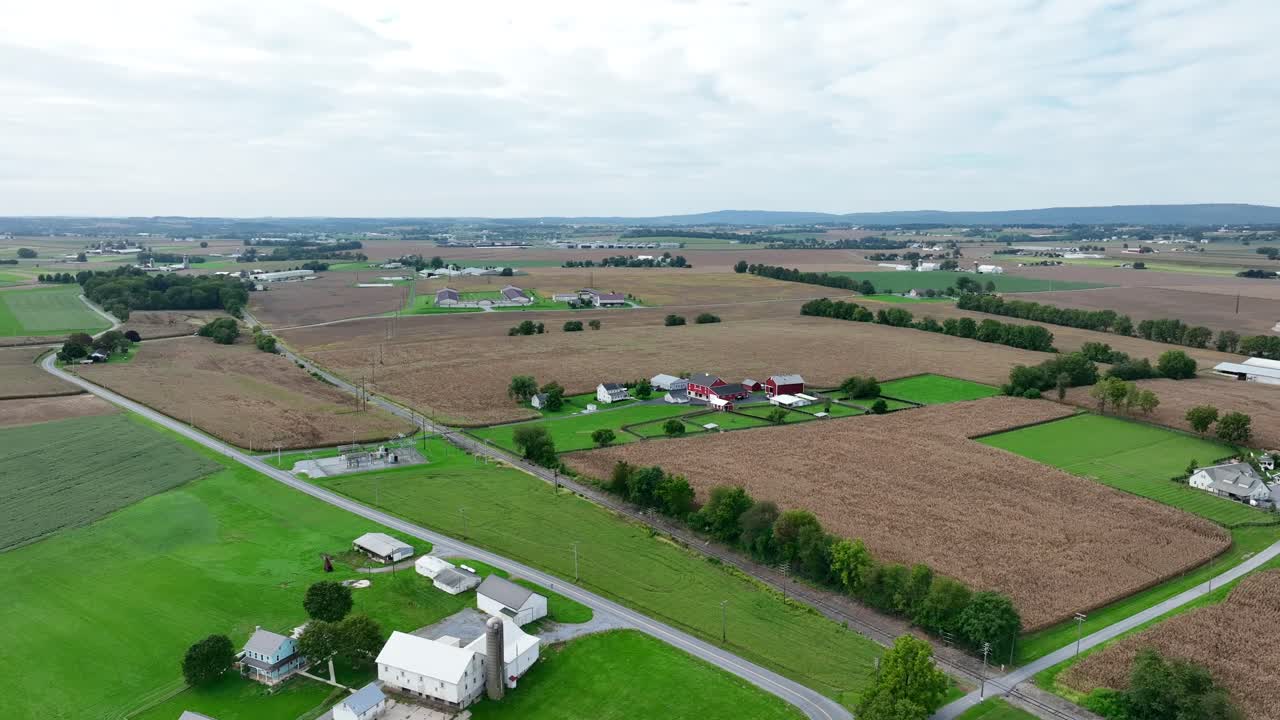 Vidtstrakt landbrugsland med lappede marker og gårde set fra luften under en overskyet himmel.