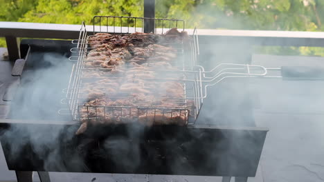 Delicious-meat-cooking-on-a-coal-grill-with-trees-on-the-background,-looking-down