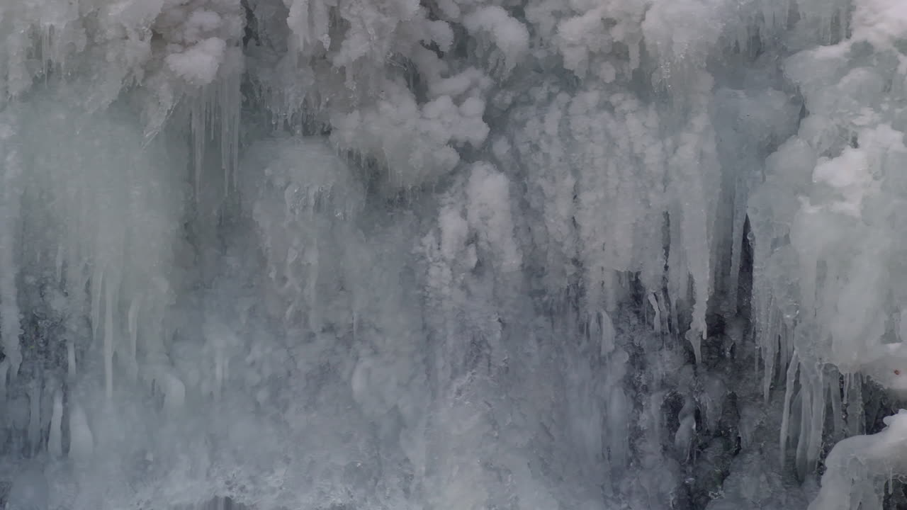 Stalattiti ghiacciate si formano su una cascata ghiacciata d'inverno mentre il ruscello continua a scorrere dietro. Scena naturale stagionale fredda, adatta per paesaggi e riprese documentaristiche.