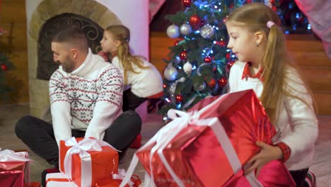 little happy girls and sisters sort out new year's gifts. a happy family near the christmas tree for the holidays. colored gift boxes