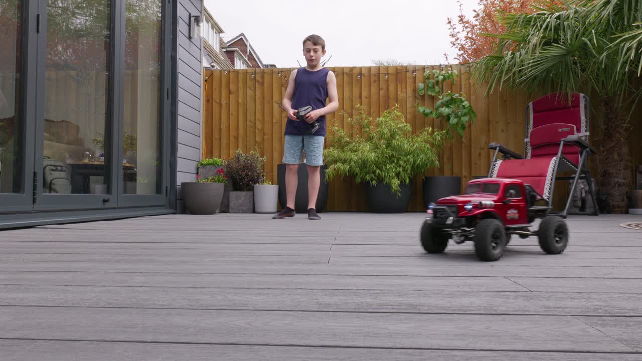 Giovane ragazzo a casa all'aperto in giardino che gioca con la sua auto RC, camion e 4x4.