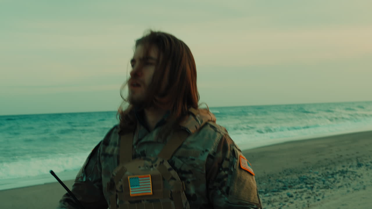 Soldato americano con i capelli lunghi cammina sulla spiaggia vicino all'oceano