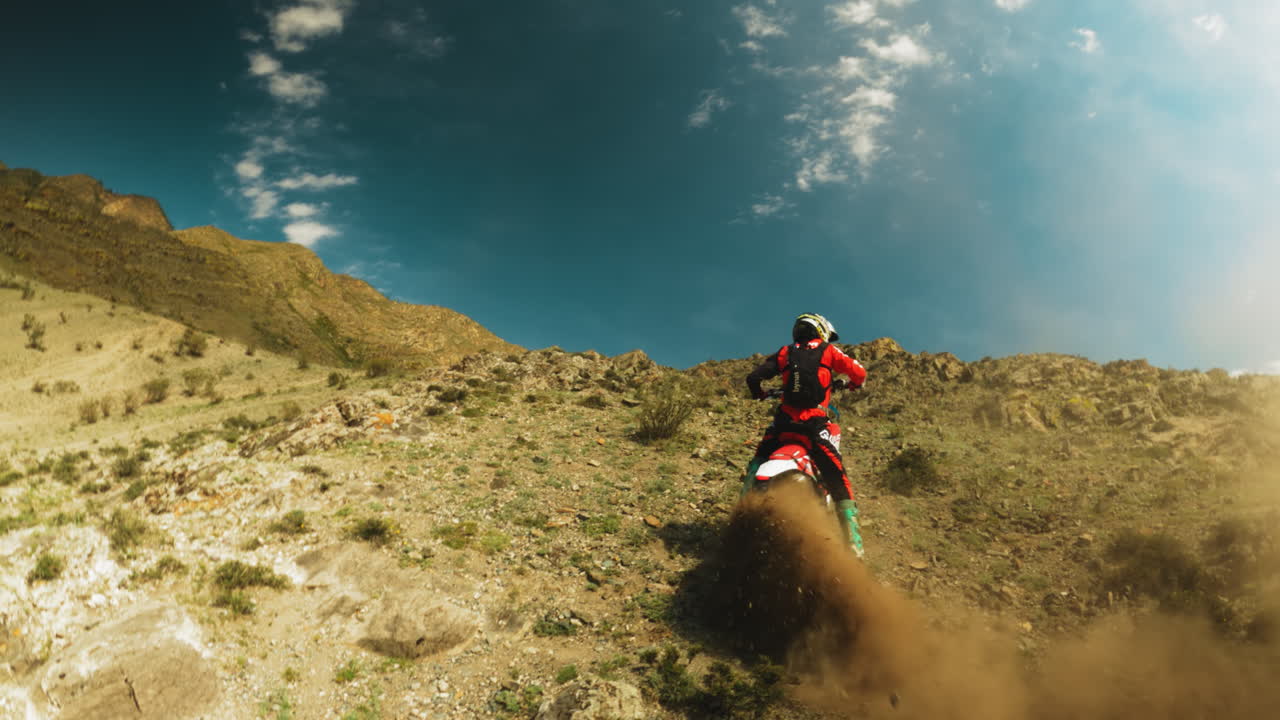 Motorcyclist on vehicle and dust cloud on slope fpv. Brave sportsman in protective uniform rides motorbike along hilly land. Extreme sport training
