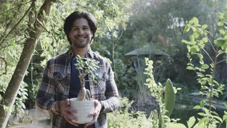 portrait of happy caucasian man holding plant in sunny garden with copy space, slow motion