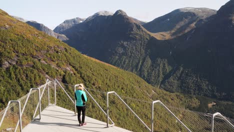 Aerial-View-of-Lonely-Female-on-Viewpoint-on-Top-of-Picturesque-Valley-in-Norway-on-Sunny-Summer-Day