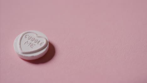 Hand-Picking-Up-Heart-Candy-With-Romantic-Message-Cuddle-Me-On-Pink-Background