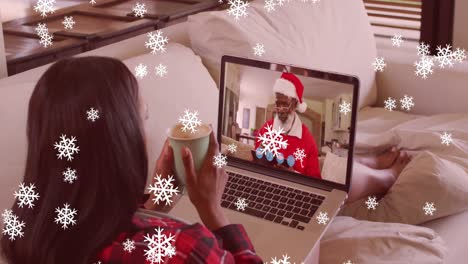 copos de nieve cayendo sobre una mujer sosteniendo una taza de café teniendo una videollamada en una computadora portátil durante la navidad