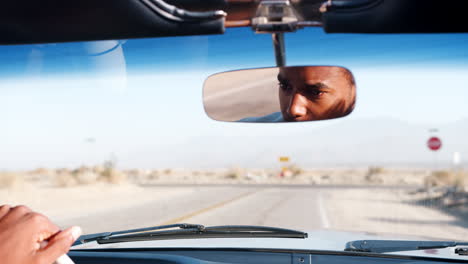 joven negro conduciendo un coche abierto, visto en el espejo retrovisor