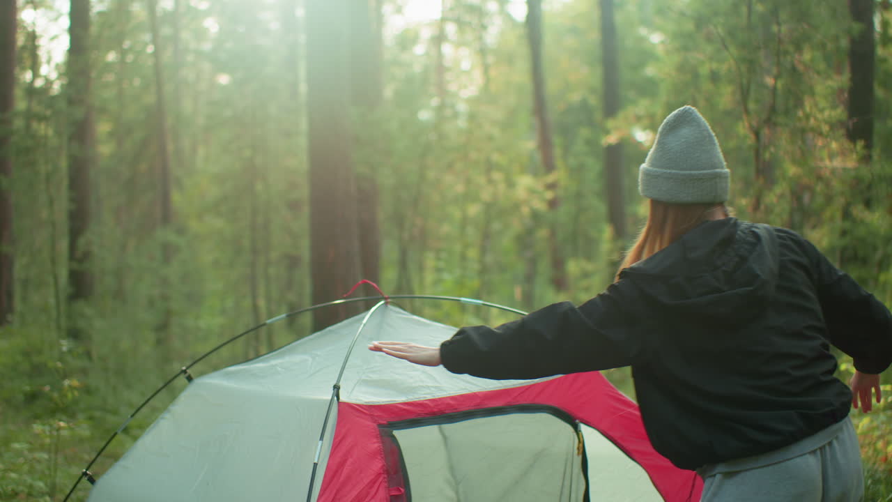 young boy watches girl as she adjusts camping tent and moves to zip it up inside forest setting surrounded by sunlight and trees during peaceful outdoor experience showcasing teamwork and focus