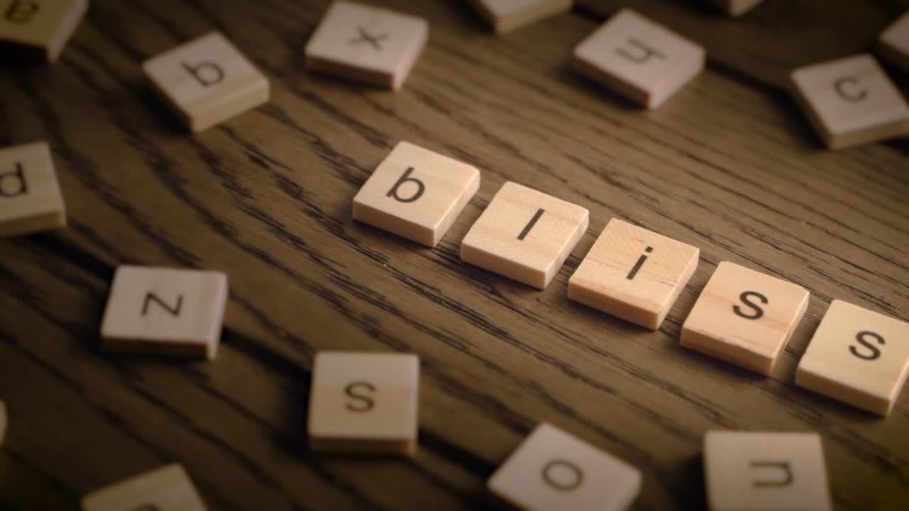 Wooden tiles spell the word bliss as the camera gently pans across a rustic wooden surface in soft, warm lighting.