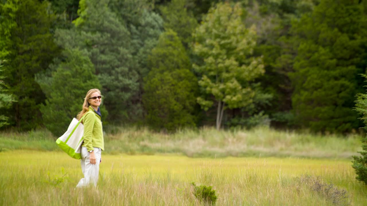 cinemagraph de una mujer bonita caminando en un prado de pastizales frente a un bosque maduro.