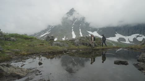 two hikers explore a misty mountain landscape with reflections in a serene pond