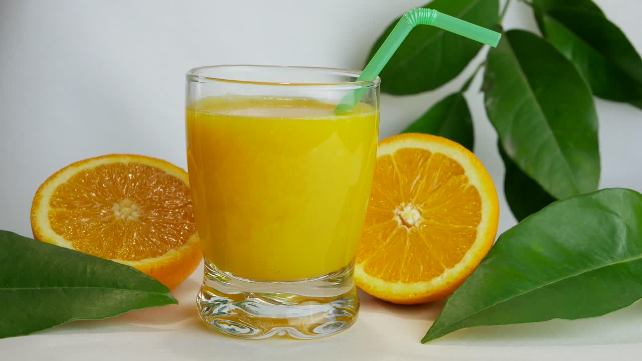 foto de estudio de un vaso lleno de jugo de naranja y mitades de naranja, primer plano, sartén lento
