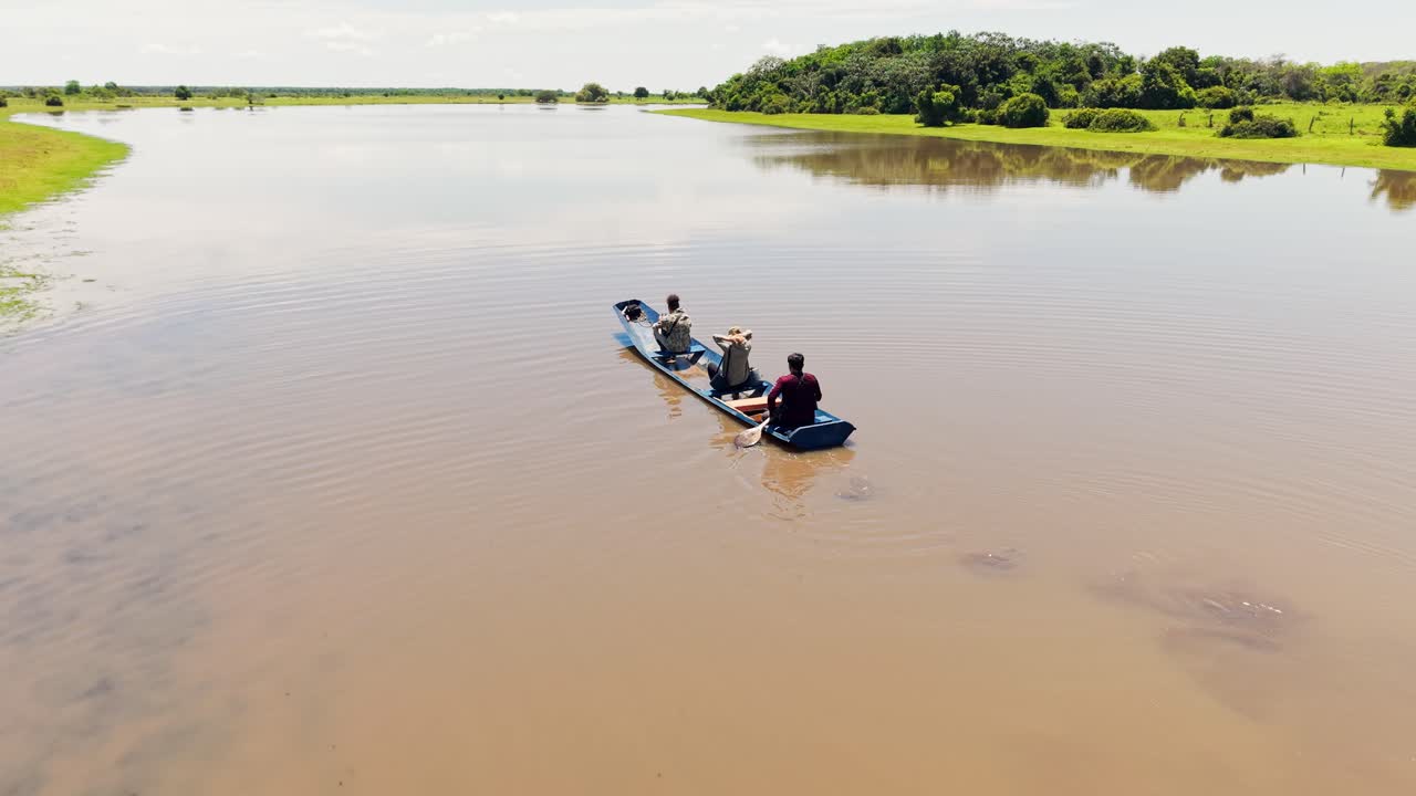 Luftfoto af folk, der navigerer en traditionel båd på en mudret flod under en llanero-safari.