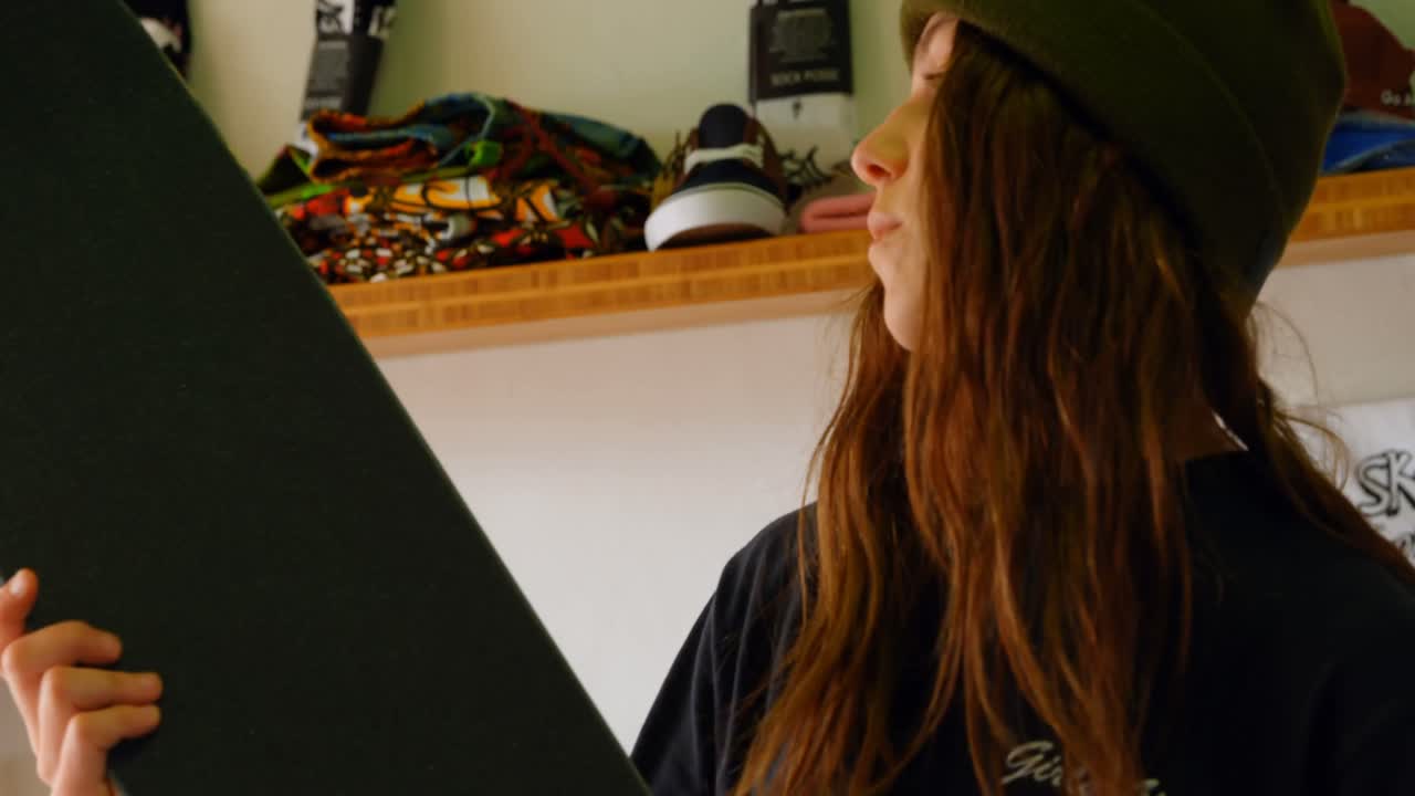 vista lateral de una joven mujer caucásica examinando la cubierta de patinaje en un taller 4k