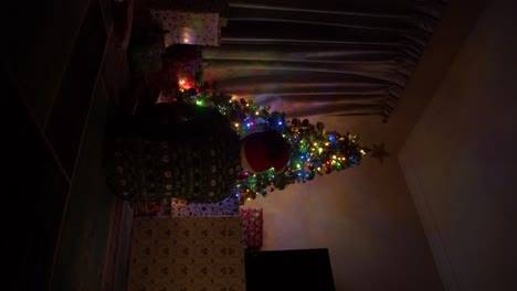 Un-Clip-Vertical-De-Un-Joven-Sentado-Frente-A-Un-Hermoso-árbol-De-Navidad-Completamente-Iluminado-Y-Decorado,-Investigando-Los-Regalos-Y-Las-Decoraciones-Como-Lo-Haría-Un-Niño-Pequeño-Antes-De-Sentarse-Y-Observar